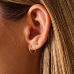 Model wearing 14K dainty twisted hoop earrings on first piercing and green tiny stud on second piercing.