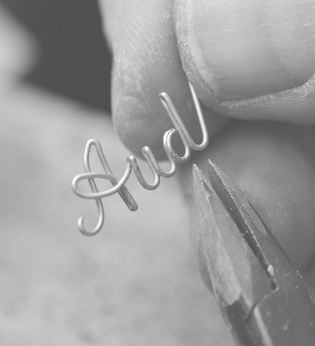 Hands holding 14K solid gold wire shaping into a custom name with pliers.