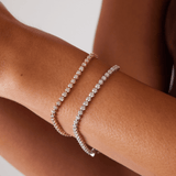 Model's wrist wearing two solid gold diamond tennis bracelets. One bracelet in 14K yellow gold and one in 14K white gold.