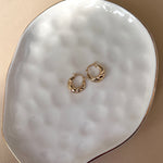 Croissant hoop earrings in 14k yellow gold flat lay on white plate.