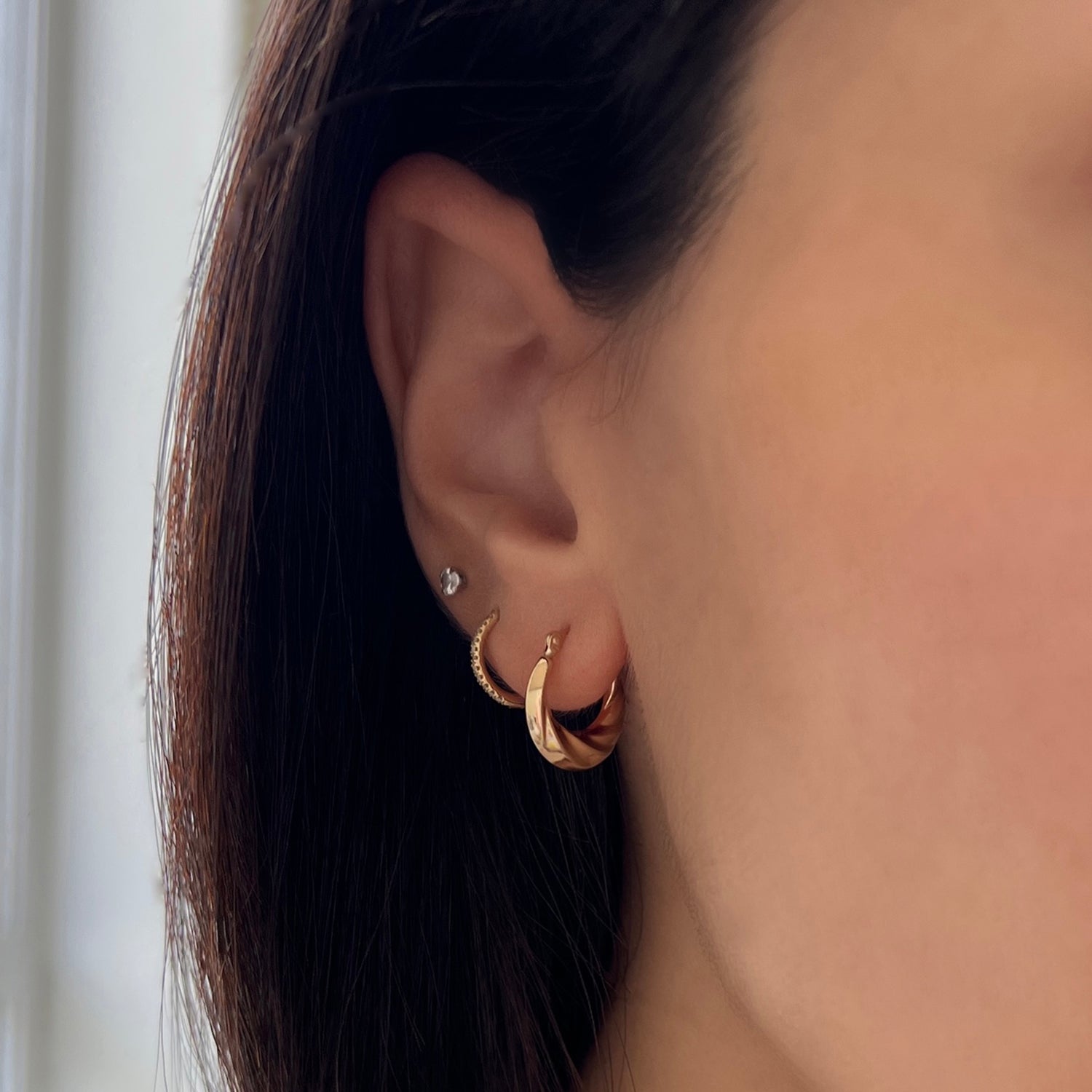 Model wearing croissaint hoop earrings in 14k solid gold on 1st piercing, huggies on 2nd piercing, and diamond stud on 3rd piercing.