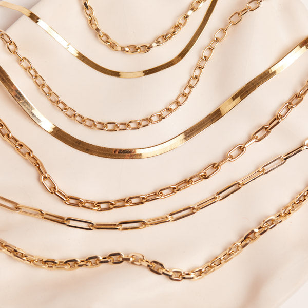 Flat lay of 14K solid gold chains including paperclip, cable chain, herringbone, chunky chains.