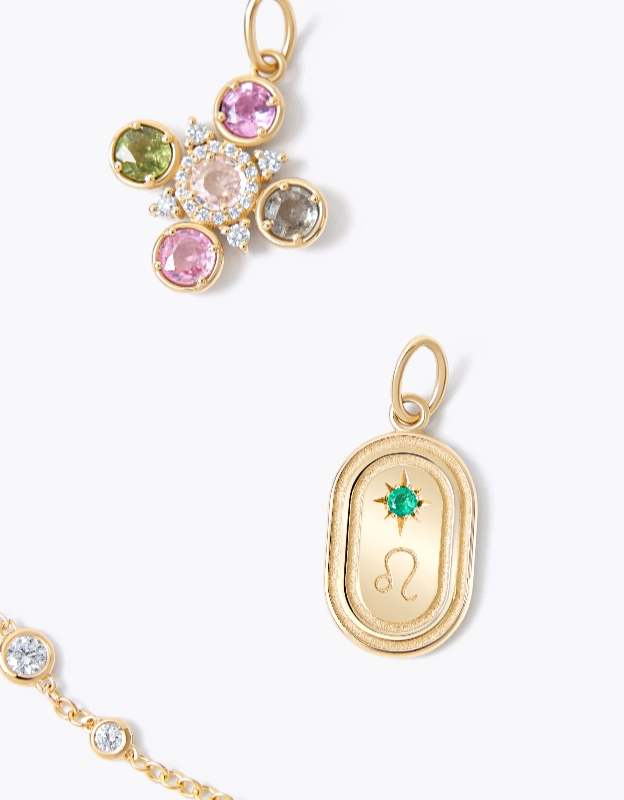 Flat lay of 14K yellow gold sapphire charm, oval starset charm, diamond bezel bracelet on a white background.