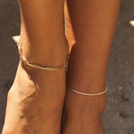 Model wearing paperclip chain anklet on one ankle and dainty pearl anklet on other ankle in 14k solid gold.