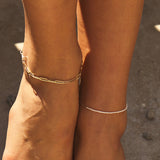 Model wearing paperclip chain anklet on one ankle and dainty pearl anklet on other ankle in 14k solid gold.