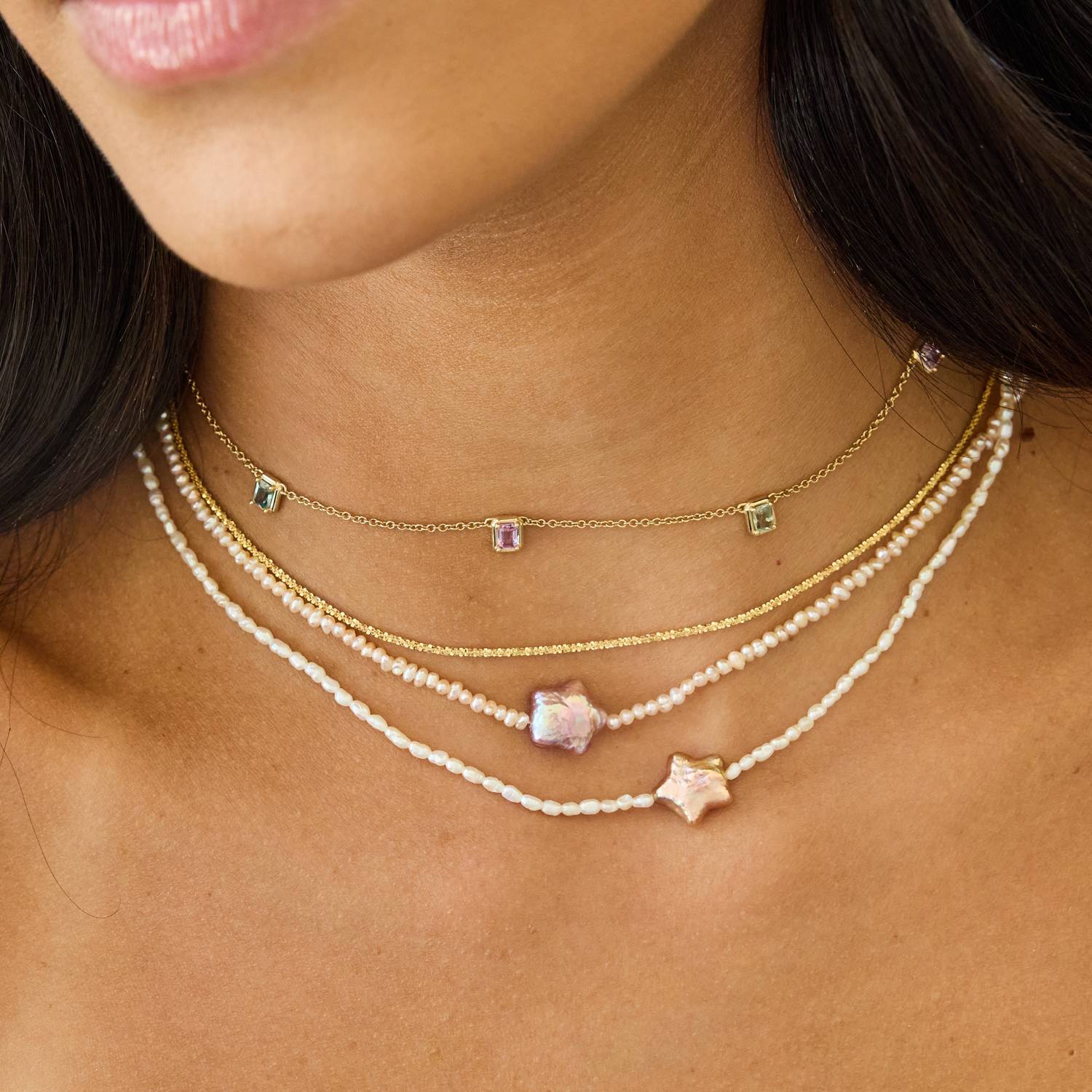 Model wearing four layered 14K solid gold and pearl necklaces. 14 inch station sapphire necklace, a solid yellow gold chain, and two pearl strand necklaces with star shaped pearl pendants.