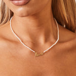 A close up on model's necklace of mini freshwater pearls with white color and nameplate in 14k solid gold that falls slightly below the collarbone.