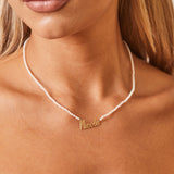A close up on model's necklace of mini freshwater pearls with white color and nameplate in 14k solid gold that falls slightly below the collarbone.