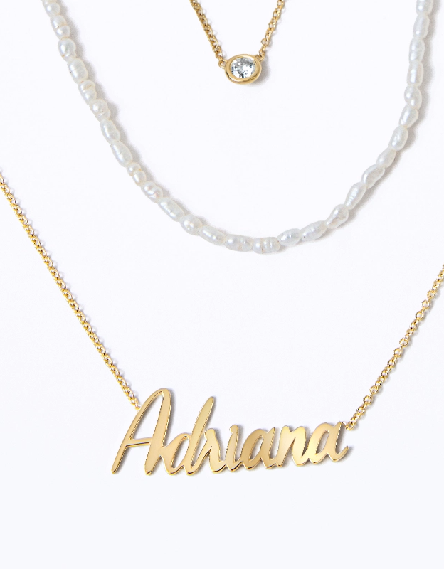 Three layered necklaces in 14K solid gold and white mini freshwater pearls. Solitaire bezel necklace, pearl strand, name necklace.