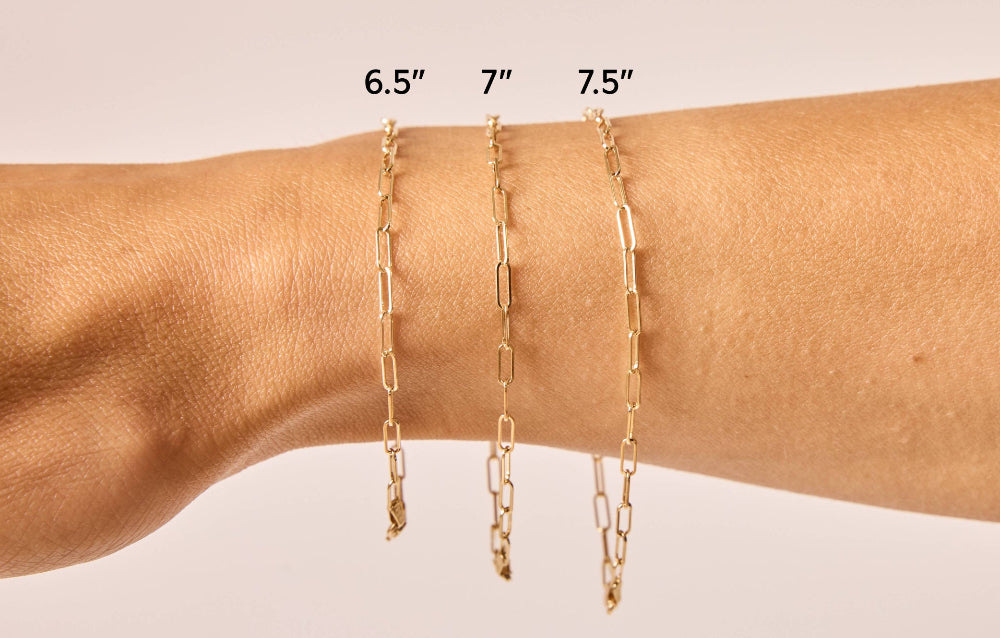 Three 14K solid gold paperclip bracelets on model's wrist in different sizes - 6.5", 7", 7.5".