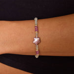 Model's wrist with aquamarine and gold beaded bracelet and star shaped purple pearl in the center.