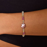 Model's wrist with aquamarine and gold beaded bracelet and star shaped purple pearl in the center.