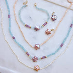 Flat lay of stella mare pearl charms, necklaces, and bracelet with aquamarine and sapphire beads, 14K solid gold, mini pearl strands, and star shaped baroque pearls.