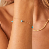 Lifestyle photo of close up on model's wrist with dainty gold chain with 3 spaced out turquoise beads on it.