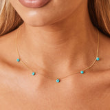 Close up shot of model's neckline with a gold chain necklace with 5 dangling turquoise beads on it.