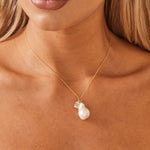 Close up shot of model wearing baroque pearl and 14k gold initial charm with 14k gold chain that falls below collarbone.