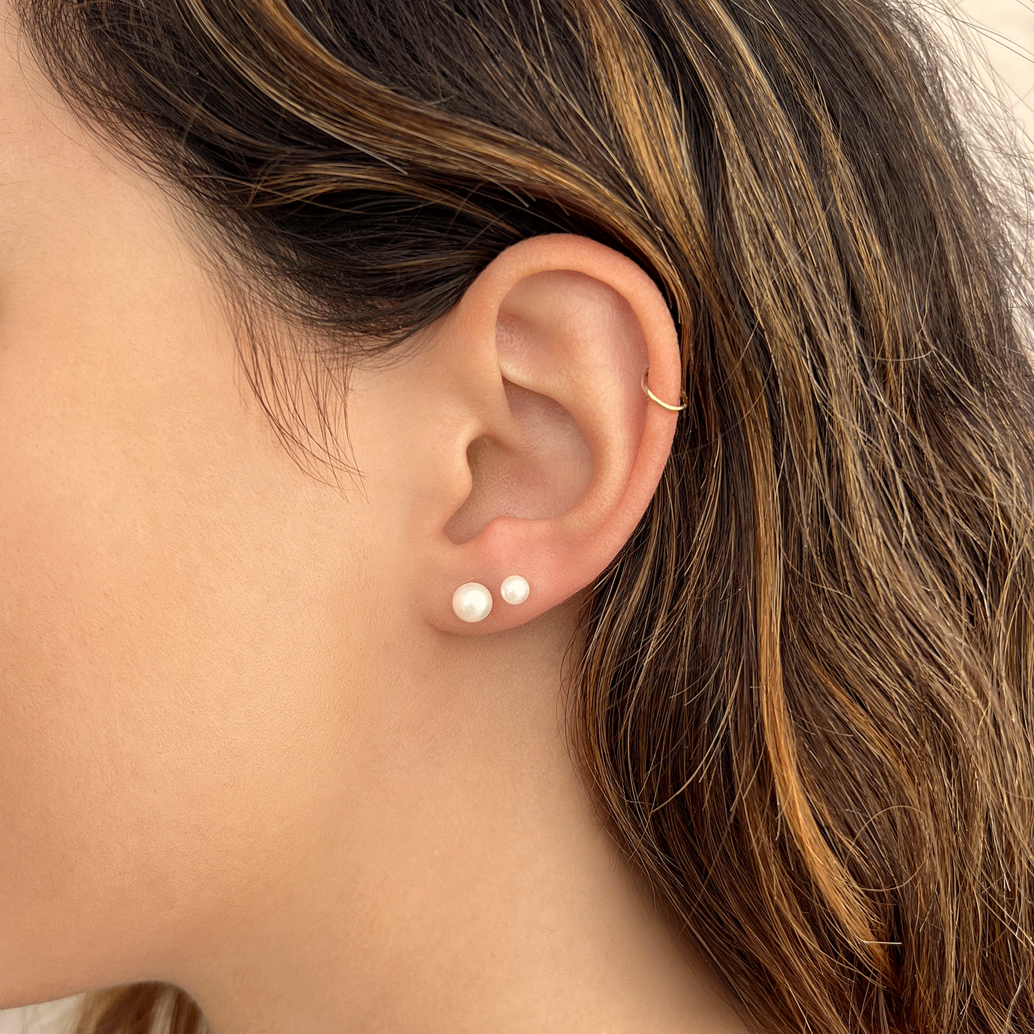 Model wearing 6mm pearl stud earring on first piercing and 4mm pearl stud earring on second piercing with 14k gold hoop on helix.